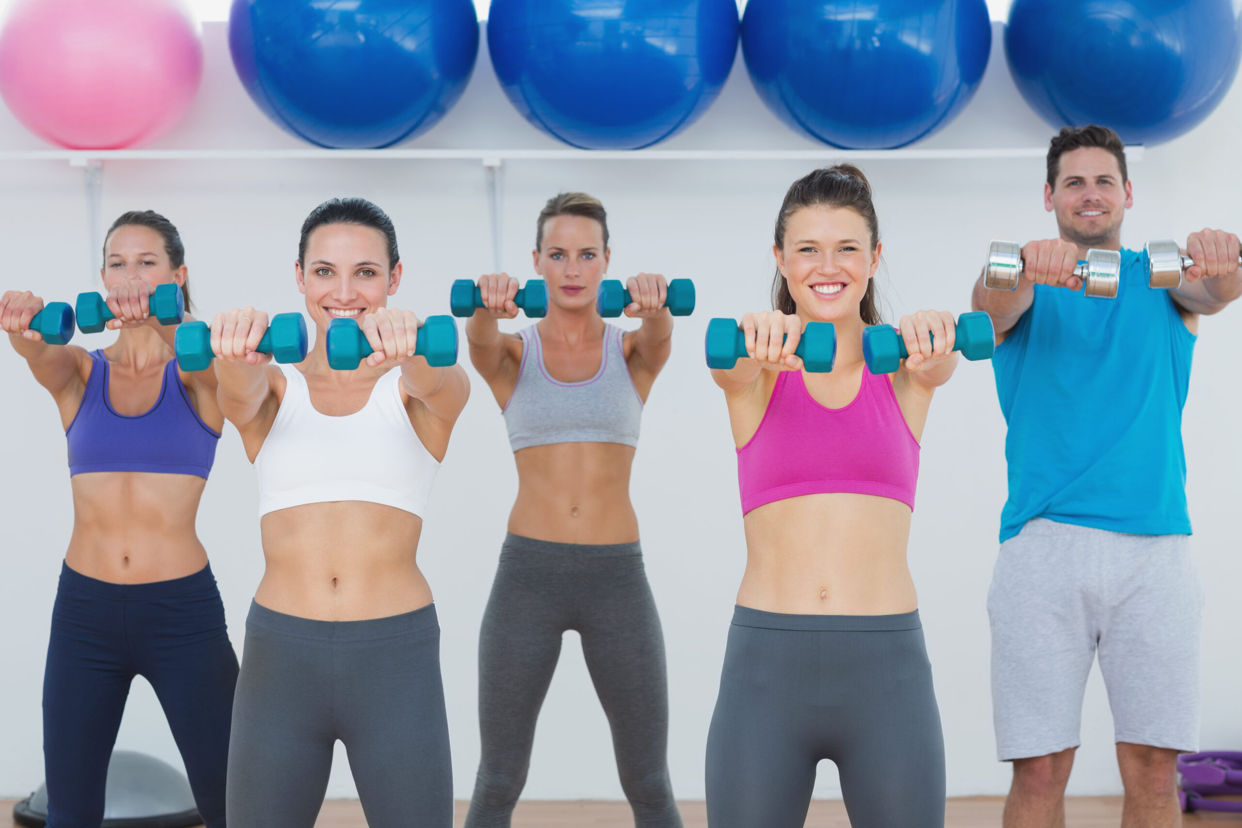 Portrait of fitness class and instructor exercising with dumbbells in the gym